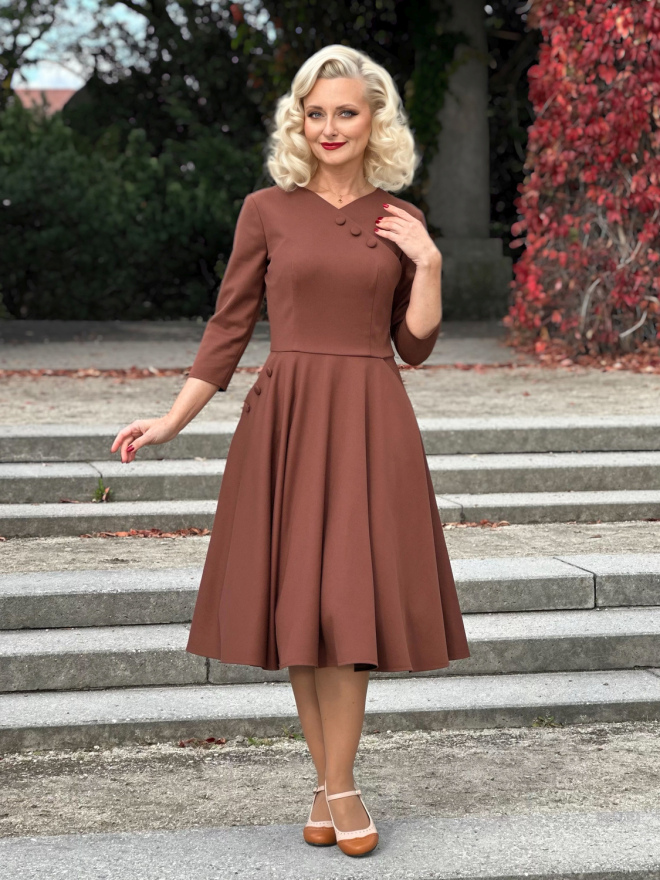 Sukienka z kopertowym dekoltem Vivian w cynamonowym brązie, z rozkloszowanym dołem i rękawami 3/4, prezentowana na modelce od przodu.